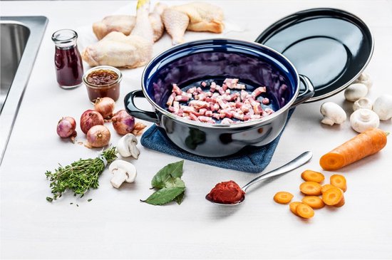 Een blauw-zwarte braadpan gevuld met spekblokjes. Ingrediënten zoals kip, uien, champignons en wortelen liggen eromheen.
