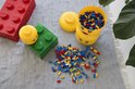 Lego opbergdozen in geel en groen, een rode Lego-bak, losse Lego-blokjes en een groene plant.