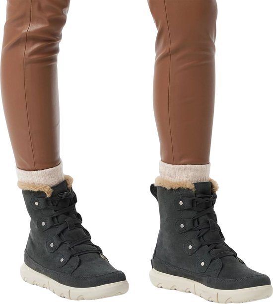 Vrouw draagt donkergrijze Sorel laarsjes met beige sokken en bruine leren broek.