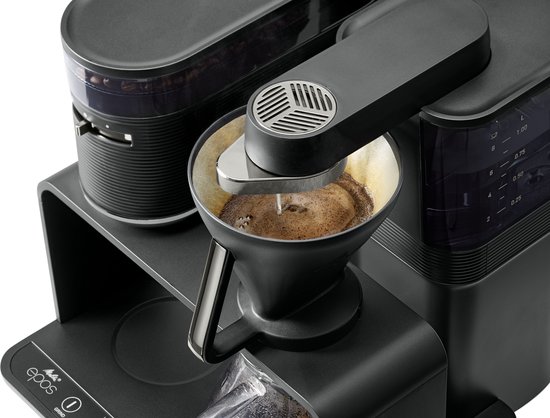 Zwart koffiezetapparaat met filter, koffiebonenreservoir en een hand die een papieren filter aanbrengt.