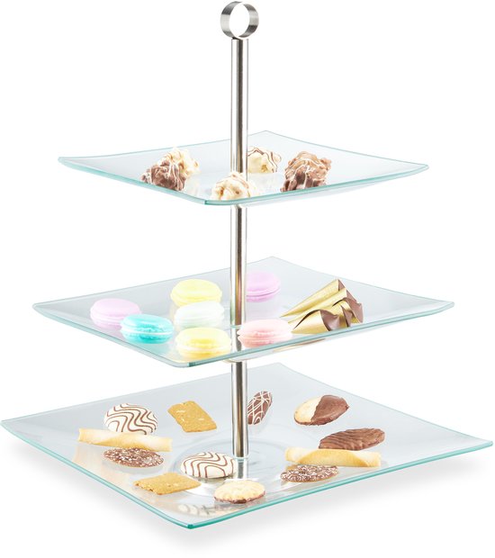 Een glazen etagère met drie vierkante plateaus, gevuld met diverse gebakjes en koekjes.