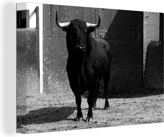 Canvas Schilderij Een zwarte stier op zand voor een deur - zwart wit - 90x60 cm - Wanddecoratie