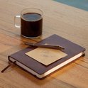 Carnet bordeaux fermé avec un stylo posé dessus. Une note disant 'Let's Connect!' est sur le carnet. Une tasse de café est à côté.