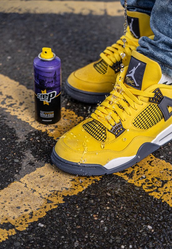 Gele sneaker op straat met gele lijnen. Waterdruppels op de sneaker. Een hand spuit met een Crep Protect spuitbus.