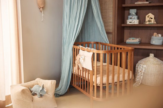 Lichtblauwe hemel met ruches boven een houten wieg in een kinderkamer.