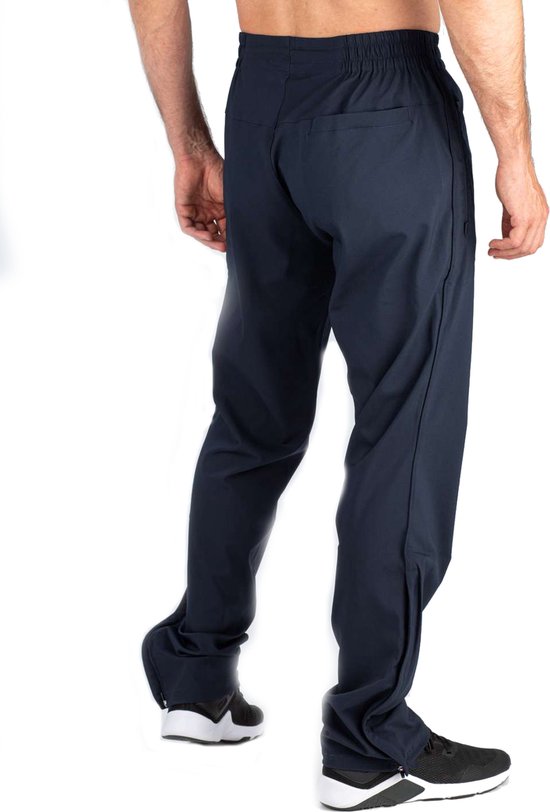 Man in donkerblauwe sportbroek met wijde pijpen en ritsjes aan de onderkant, gedraaid naar de zijkant.