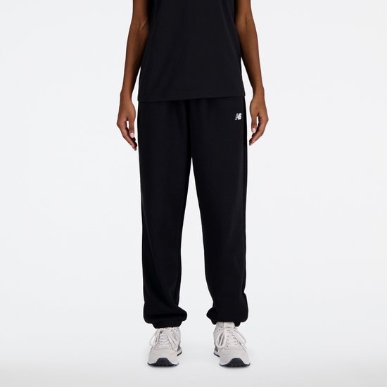 Zwarte New Balance joggingbroek met wit logo, gedragen met witte sneakers.