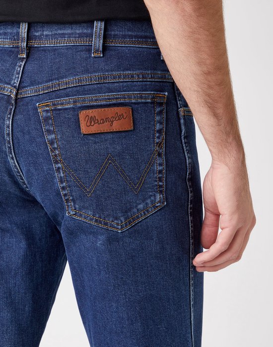 Close-up van de achterkant van een donkerblauwe Wrangler jeans met oranje stiksels en Wrangler-patch.