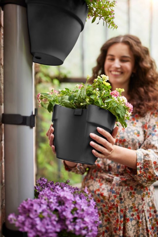 Vrouw met krullend haar houdt een donkergrijs regenpijpbakje vast, klaar om deze op de regenpijp te bevestigen.
