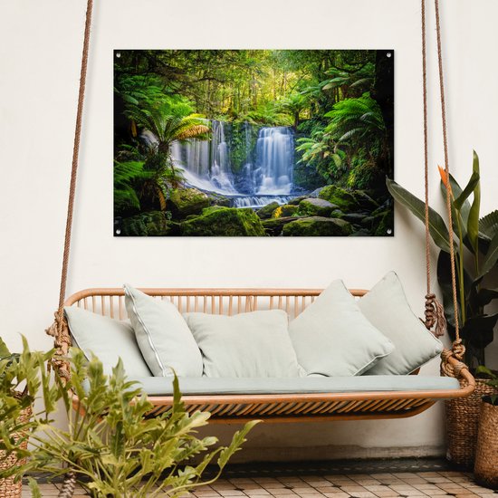 Waterval in een groen bos met varens en mos, hangend boven een loungeset.