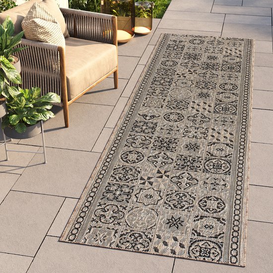 Tapis de couloir avec un imprimé mosaïque beige et noir, posé sur une terrasse carrelée à côté de meubles de jardin.