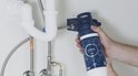 Handen bevestigen een blauwe GROHE BLUE S-SIZE waterfilter aan een gootsteenafvoerbuis.