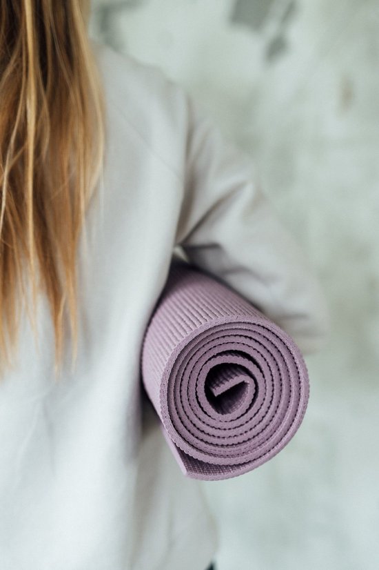 Een vrouw draagt een opgerolde lavendelpaarse yogamat.