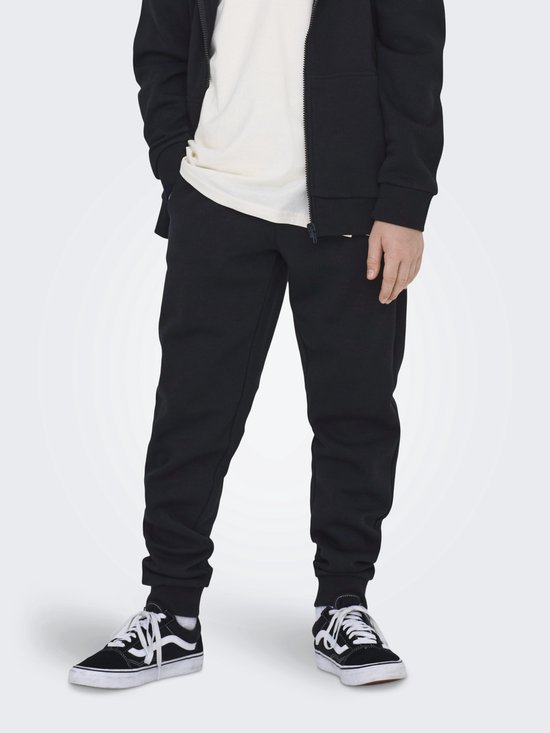 Jongen in een zwarte joggingbroek en beige T-shirt.
