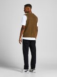 Man, achterkant, draagt bruin gebreid vest over wit t-shirt en zwarte jeans.