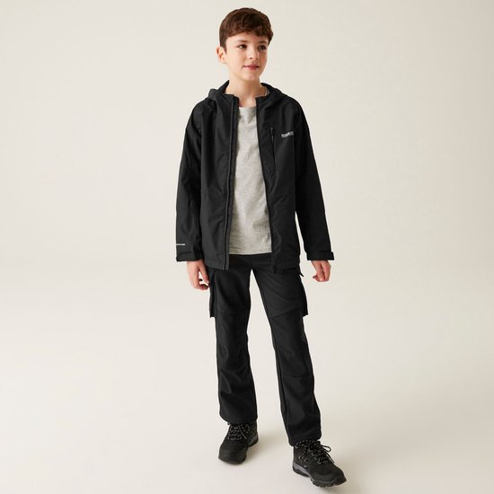 Jongen in zwarte waterdichte jas met capuchon, grijs T-shirt en zwarte cargo broek.