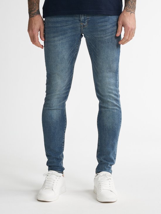 Gezicht op de benen van een man in een blauwe skinny jeans en witte sneakers.