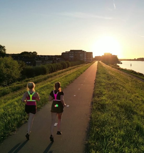 Twee vrouwen hardlopend bij zonsondergang, beiden dragen een geel reflecterend hardloopvest met LED-verlichting.