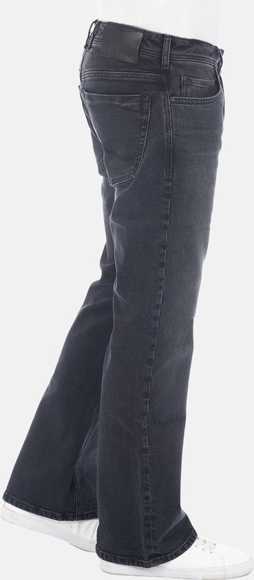 Zijaanzicht van een donkergrijze spijkerbroek met bootcut pasvorm, gedragen met witte sneakers.