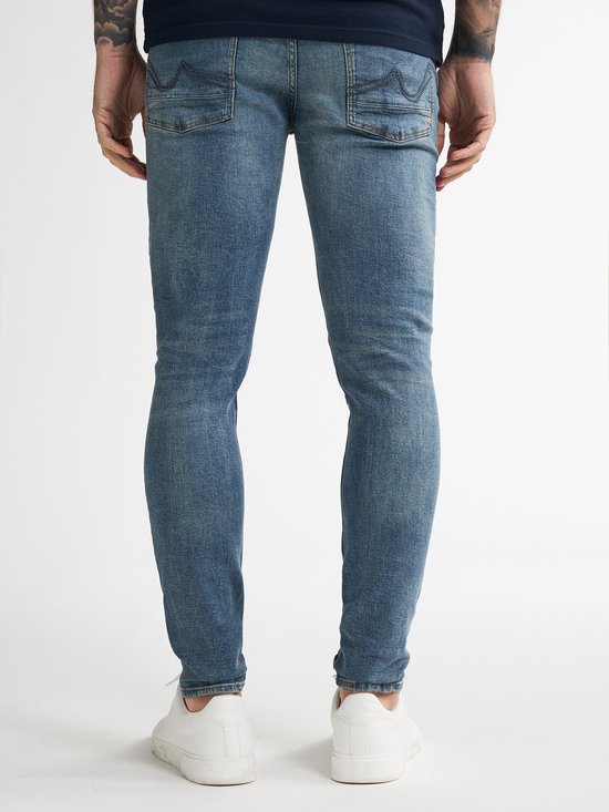 Twee mannen, van achteren gezien, staand in blauwe skinny jeans en witte sneakers.