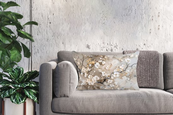 Coussin avec des branches de fleurs blanches et dorées sur un canapé gris avec un jeté.