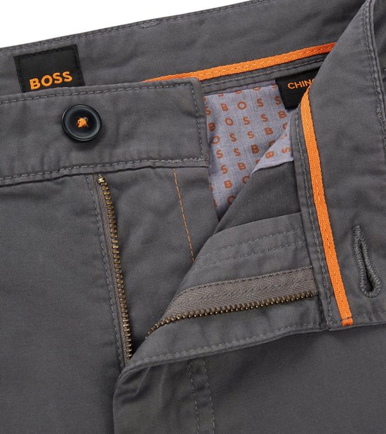 Detail van de knoopsluiting van een antracietkleurige BOSS chino met rits. De binnenkant van de tailleband heeft een oranje voering en BOSS-logo.