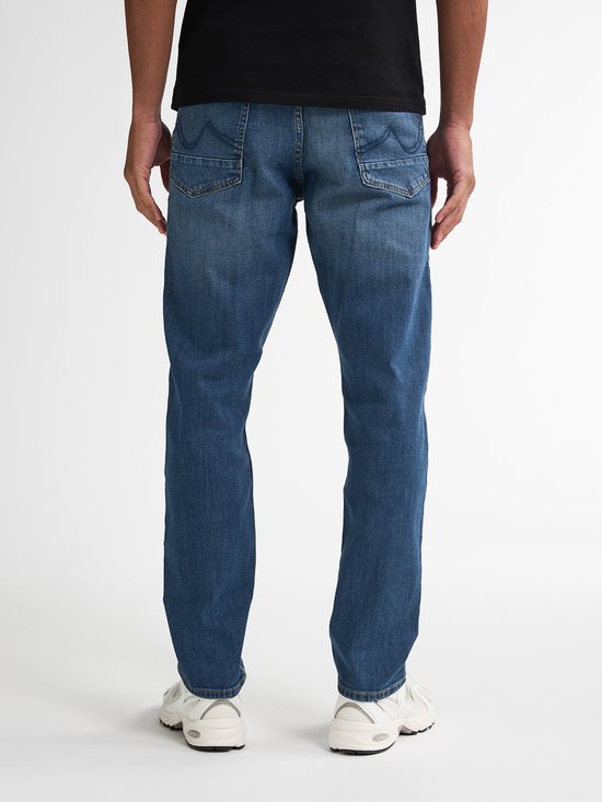 Achterkant van een man met een zwarte top en een spijkerbroek. De broek is blauw met een lichte wassing.