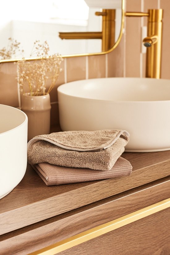 Deux chiffons de nettoyage couleur taupe sur un meuble de salle de bain en bois, dont un avec une structure côtelée.