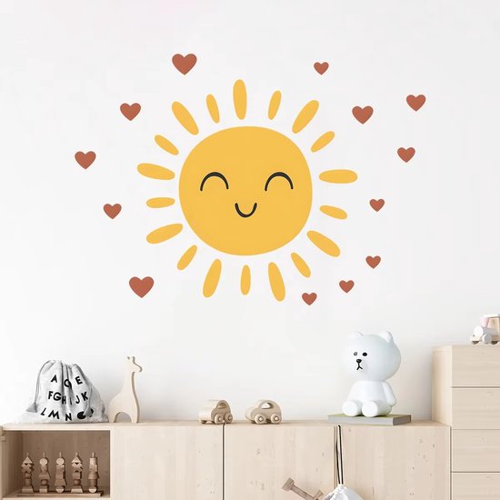 Sticker mural soleil jaune souriant avec cœurs marron, au-dessus d'une commode en bois avec des jouets.
