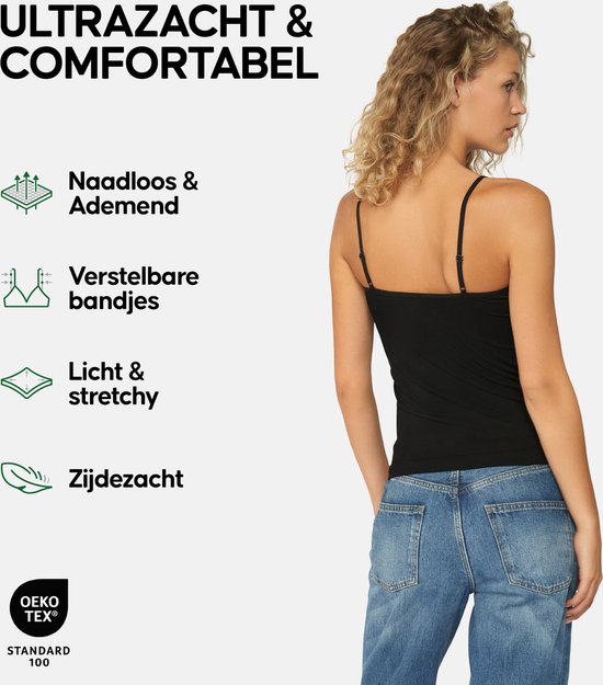 Achterkant van een vrouw met krullend blond haar in een zwart hemdje met spaghettibandjes en een spijkerbroek.