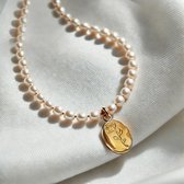 Parelketting met gouden medaillon met roosafbeelding op een glanzende witte zijden stof.