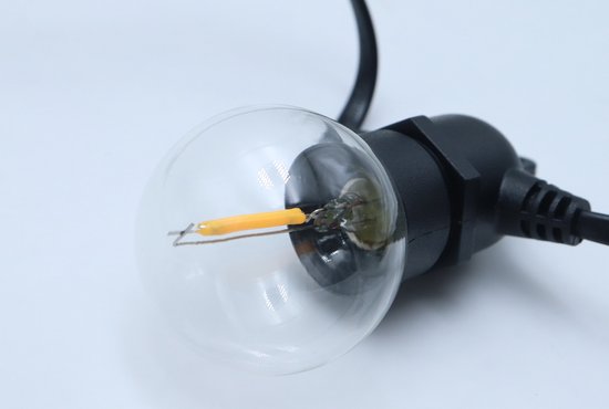 Close-up van een transparant, rond LED-lampje met een geel filament op een zwarte fitting.