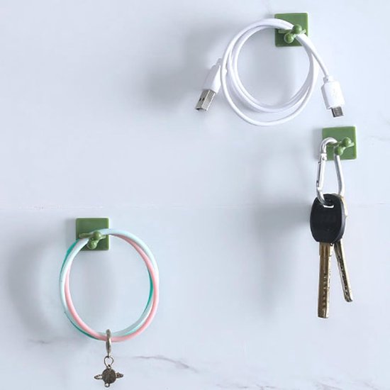 Groene clips aan een witte muur houden een opgerolde witte kabel, een sleutelbos en een roze/groene armband vast.