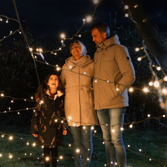 Familie van drie rond kerstlichtjes, kijkend in de verte.