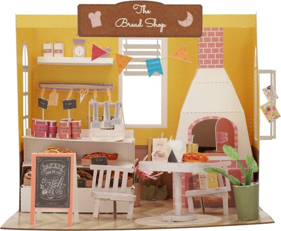 Gele miniatuur broodwinkel met bakkerij-items op toonbank, oven, tafeltje en plant.