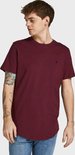 Man met tatoeages op zijn arm draagt een bordeauxrode t-shirt met korte mouwen en ronde hals, met een klein logo op de borst, staand.
