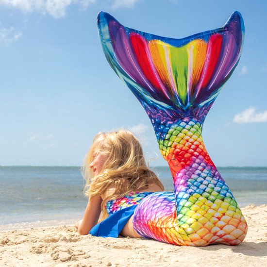 Een jong meisje met blond haar liggend op het strand, met een felgekleurde regenboog zeemeerminstaart.