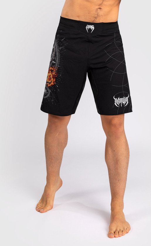 Man met zwarte Venum sportbroek met vlammenprint op linkerbroekspijp en VENUM-logo op rechterbroekspijp.