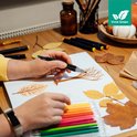 Handen met Vivid Green markers, maken tekening van boom, met herfstbladeren en potloodset.