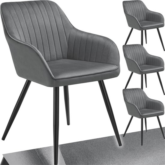 Grijze fluwelen stoel met gestikt patroon en zwarte poten, met drie kleinere stoelen op de achtergrond.