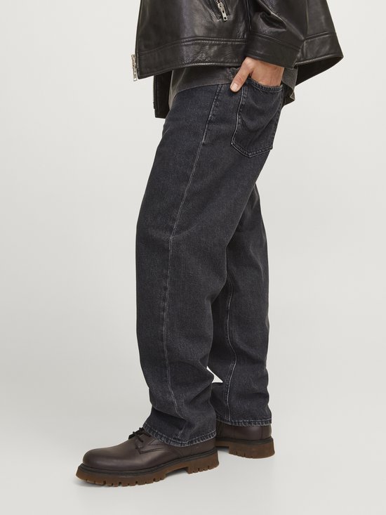 Model draagt losse, zwarte jeans met leren jack.