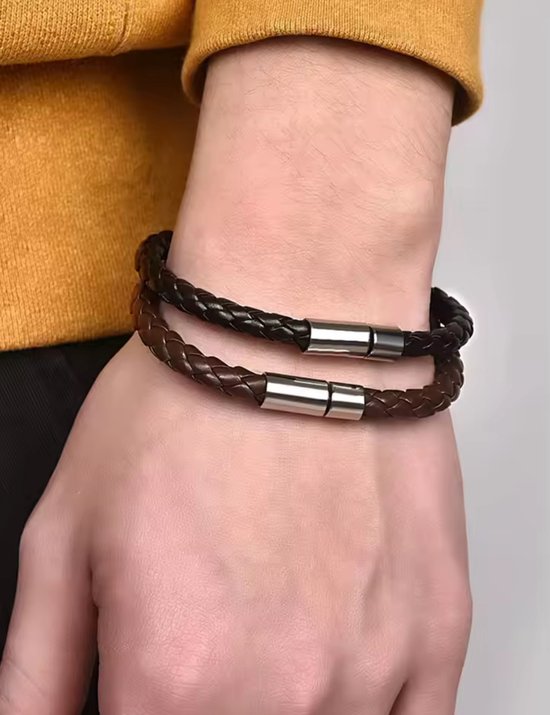 Een pols met twee gevlochten leren armbanden, zwart en bruin, met zilverkleurige magneetsluitingen.