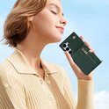 Femme tenant un étui de téléphone vert foncé avec fermeture éclair et bandoulière.