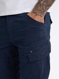 Donkerblauwe cargobroek met klepzak op het been, zichtbare tatoeage op de arm.
