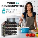 Vrouw met schort die een kruidenpotje strooit in een keuken, met een kruidenrek gevuld met 24 potjes.