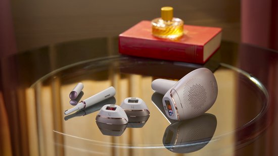 Wit Philips Lumea IPL ontharingsapparaat met rosé gouden accenten, twee opzetstukken en precisietrimmer op een glazen tafel.