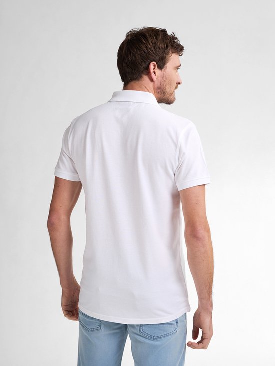 De achterkant van een witte polo met een klein logo op de linkerborst, gedragen door een man met een lichte spijkerbroek.