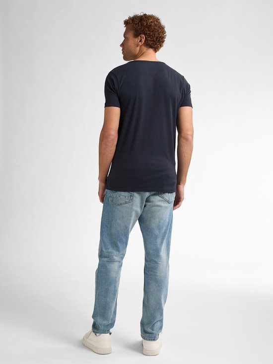 Man met krullend rood haar, sproeten, zicht van achteren in donkerblauw t-shirt en lichte spijkerbroek.