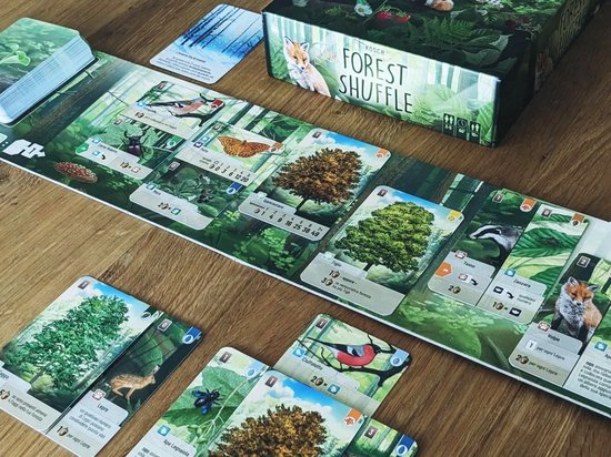 Spel van Forest Shuffle op een houten tafel. Toont spelbord, kaarten met bomen en dieren, en de speldoos.