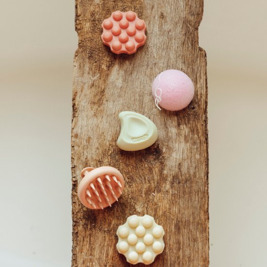 Vijf Wondr producten op een houten plank: vier massageborstels en één sponsje.